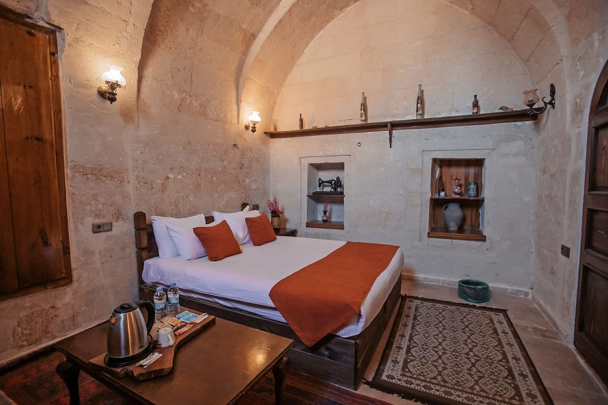 A cozy room with a bed, wooden furniture, a shelf with bottles, and a wall-mounted shelf with decorative items.