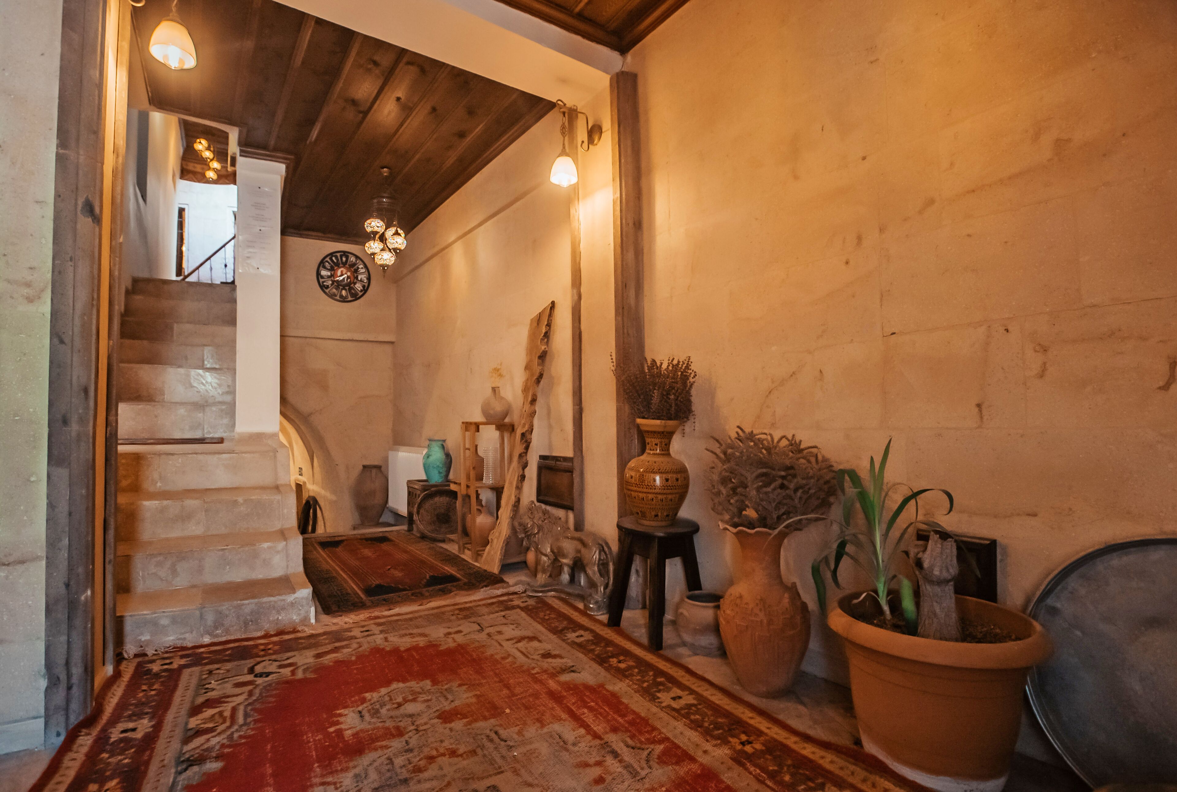 Un escalier menant à un deuxième étage, un tapis rouge à motifs et divers objets décoratifs, notamment des vases et une plante en pot.