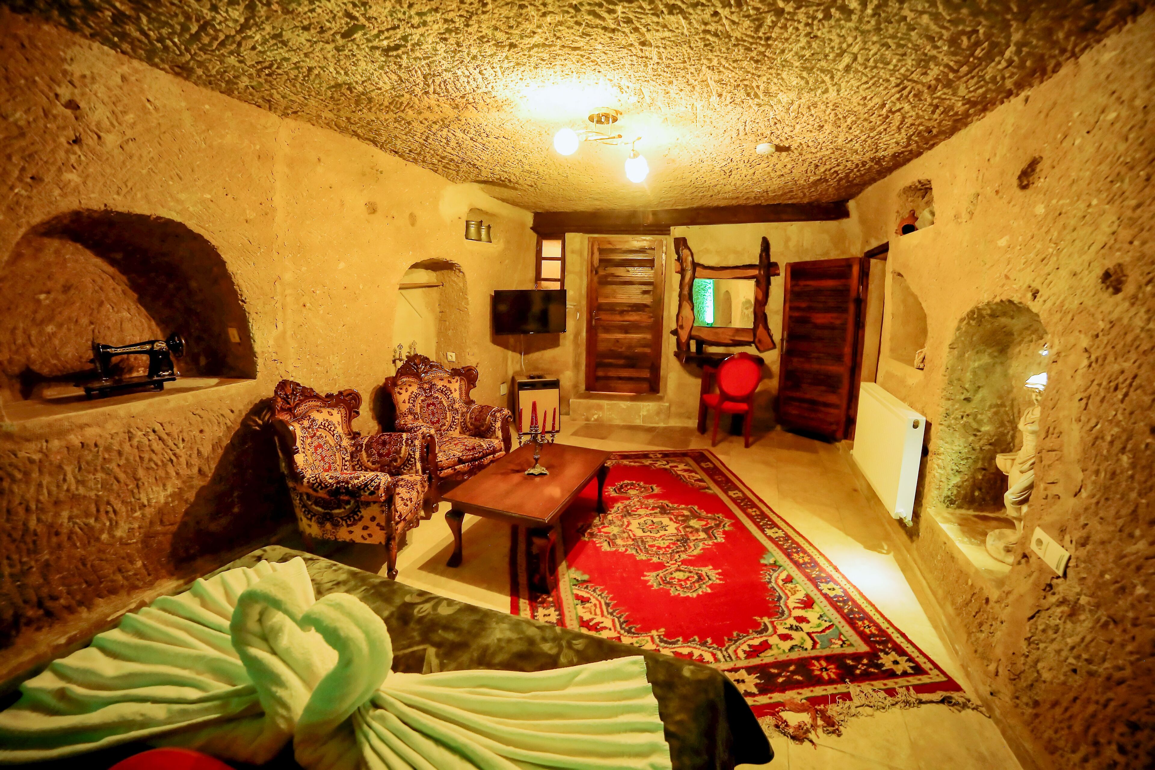 A rustic room with stone walls, a wooden door, a television, a patterned sofa, and a red carpet.