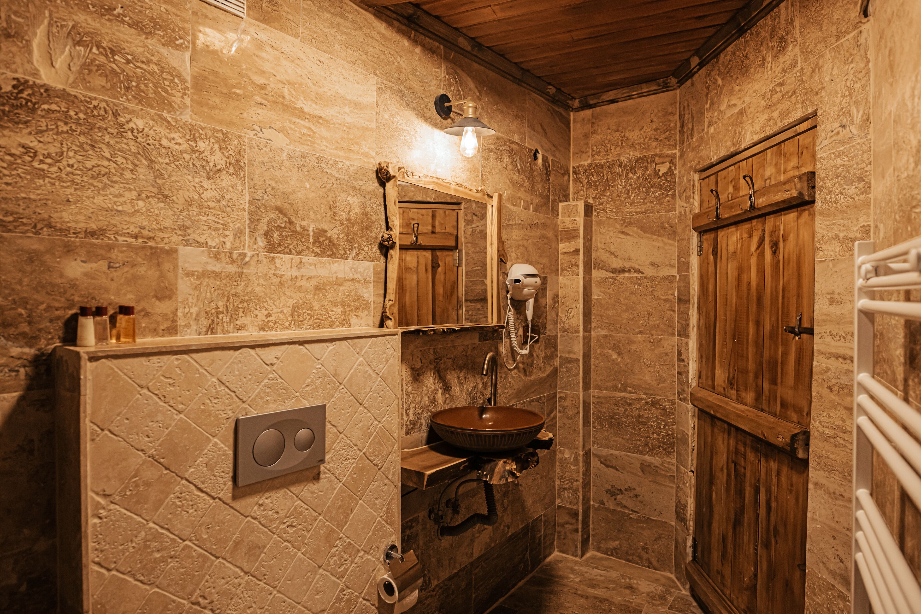 Un baño rústico con pared de piedra, puerta de madera y lavamanos empotrado.
