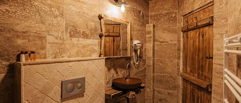 Un baño rústico con pared de piedra, puerta de madera y lavamanos empotrado.