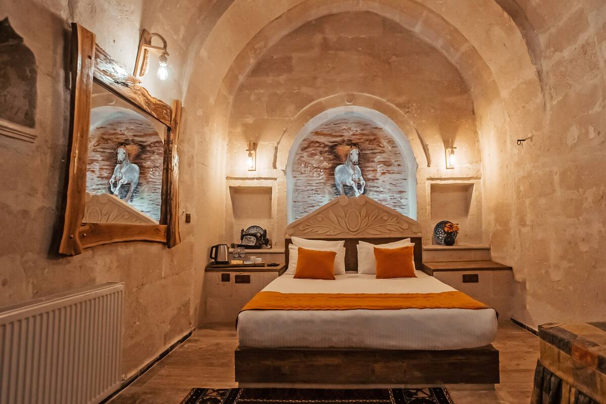 A bedroom with a large bed, two nightstands, a mirror, and a wall-mounted light fixture.