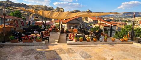 An outdoor seating area with tables and chairs, potted plants, and a view of a mountainous landscape.
