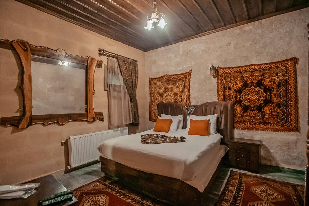 A bedroom with a large bed, a wooden headboard, a mirror, a radiator, a nightstand, and a patterned rug.