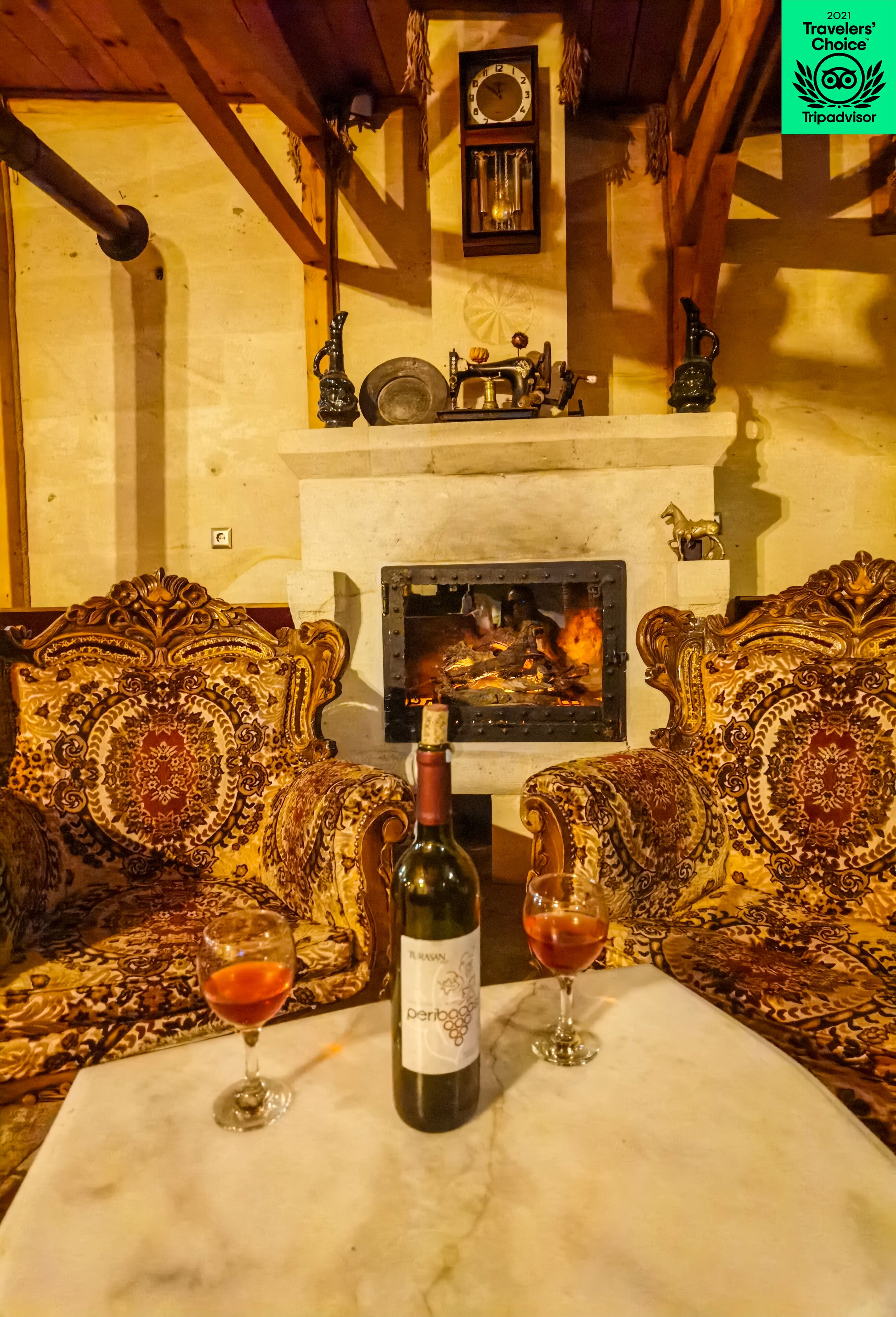A cozy room with ornate sofas, a fireplace, and a bottle of wine on a table.