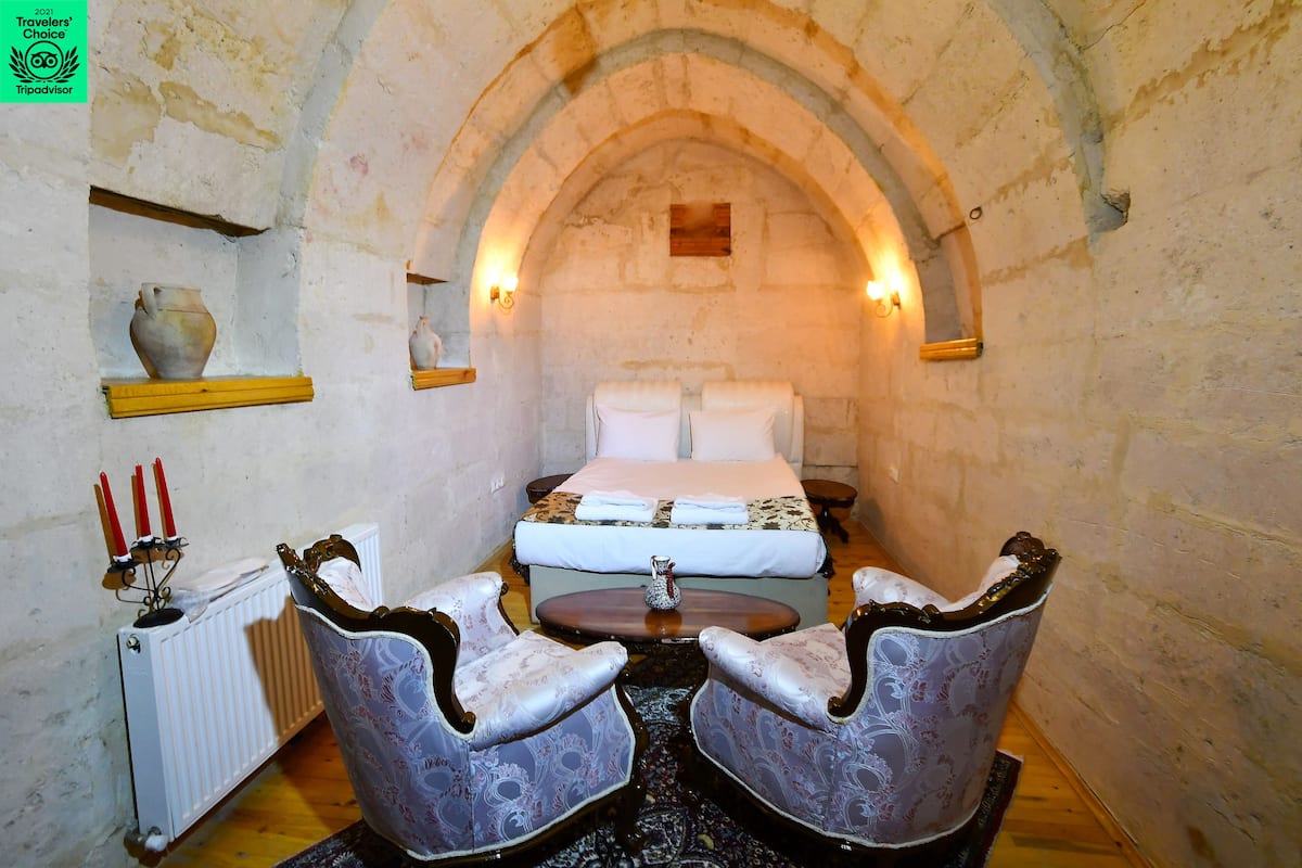 A room with a bed, two chairs, a table, a radiator, and wall-mounted lights.