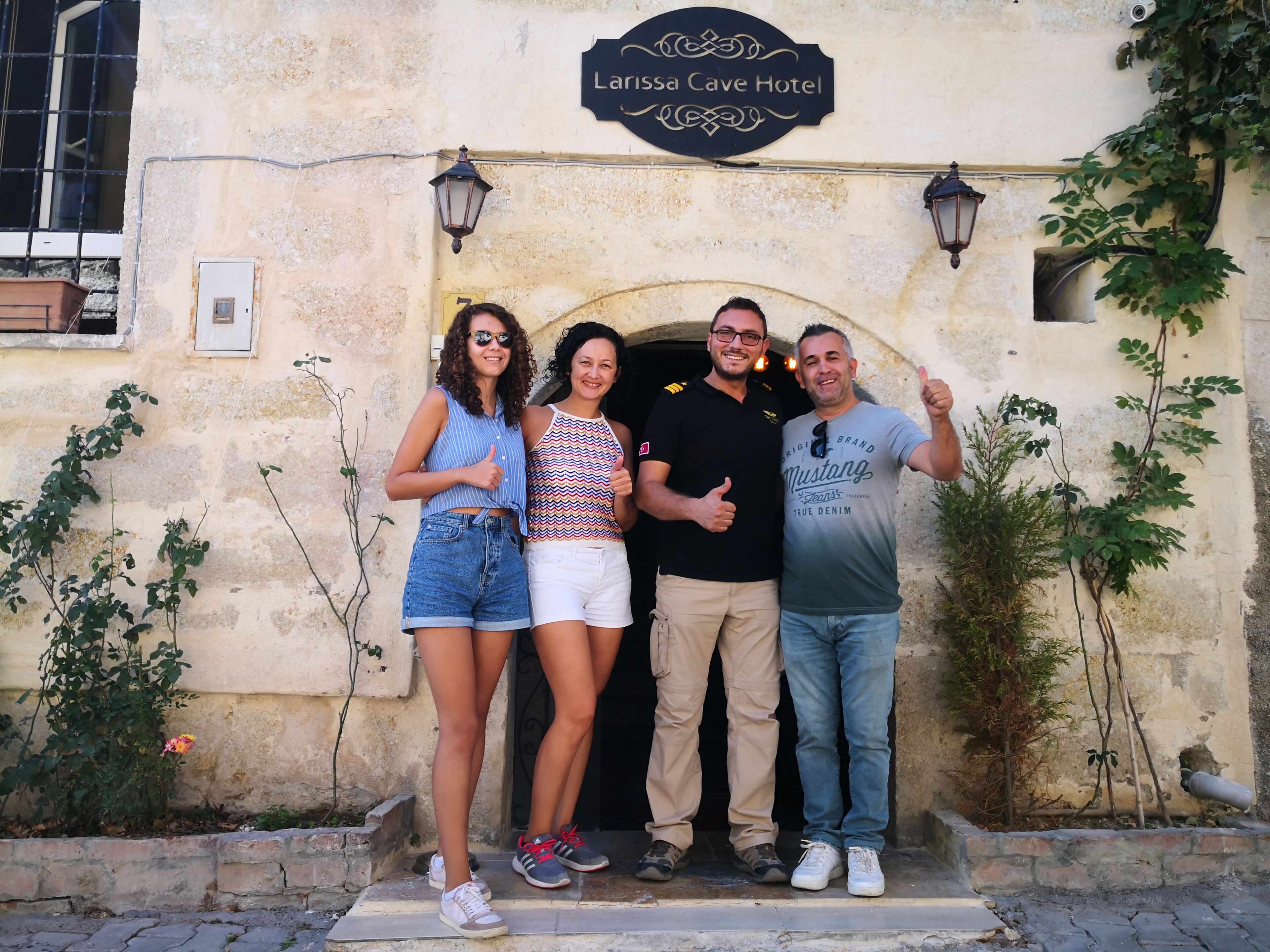 A group of people standing in front of a building with a sign that reads "Larissa Cave Hotel".