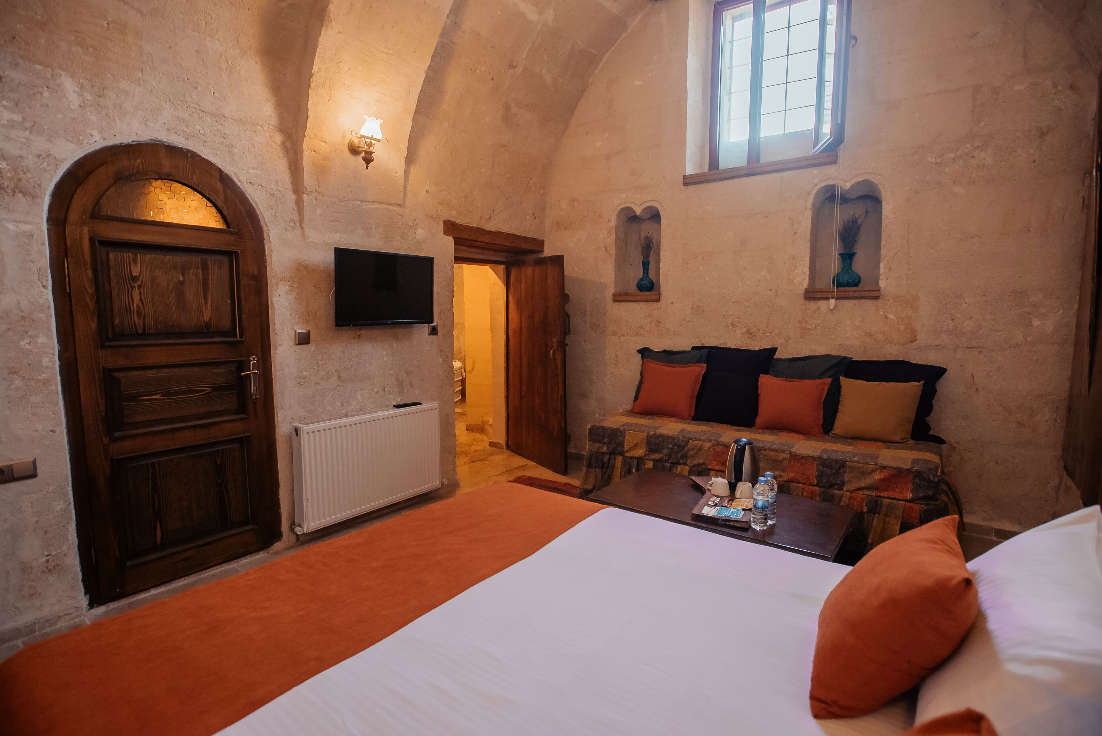 A bedroom with a large bed, a wooden door, a television, and a small window.