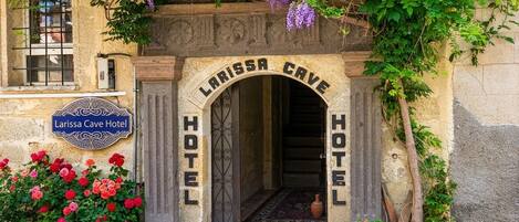 The entrance to the Larissa Cave Hotel with a stone archway and a sign above it.