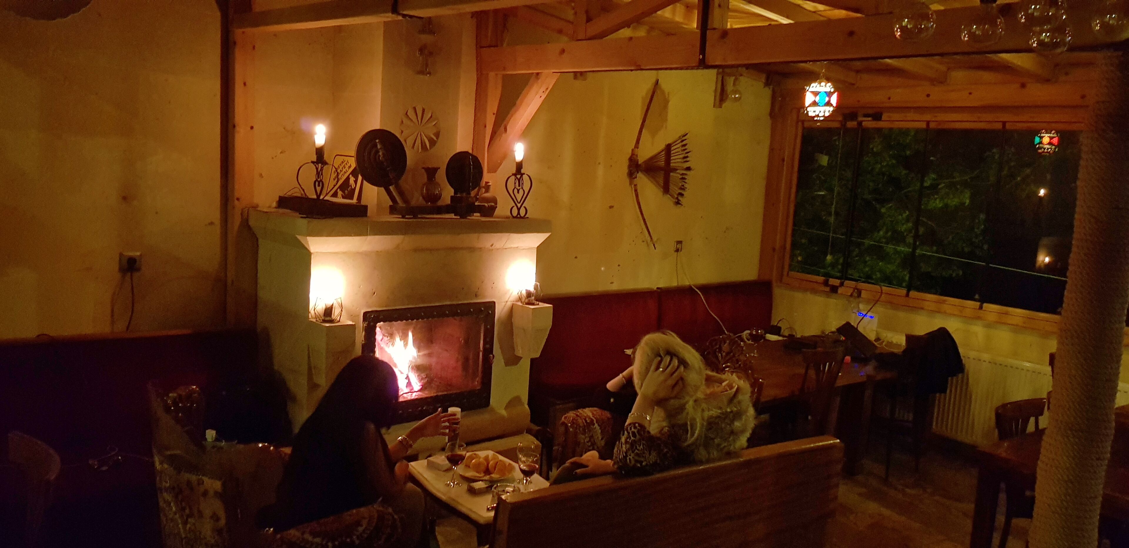 A cozy room with a fireplace, wooden beams, and a view through a window.