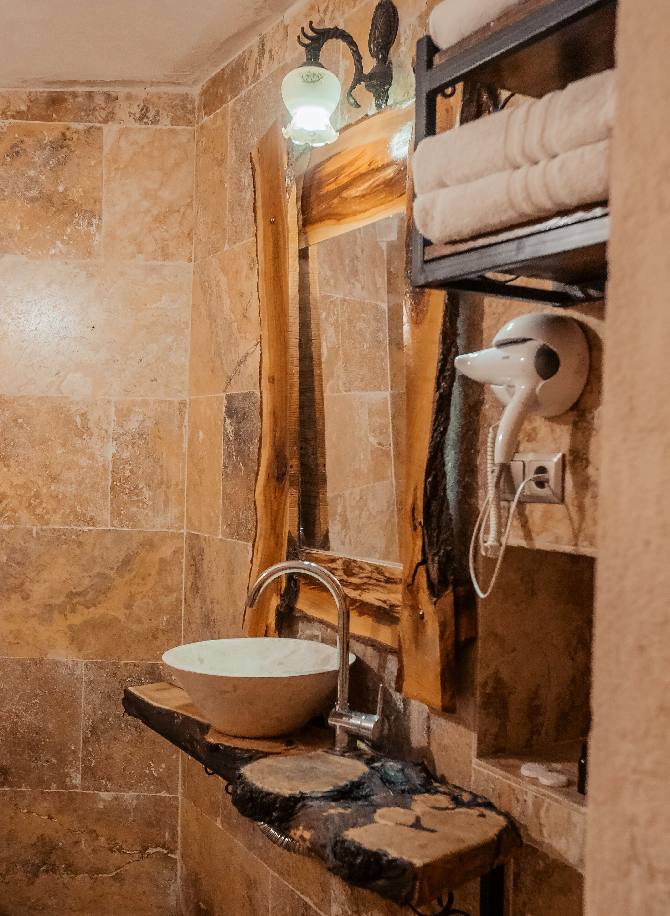 A bathroom with a stone sink, a wooden shelf, and a hairdryer mounted on the wall.