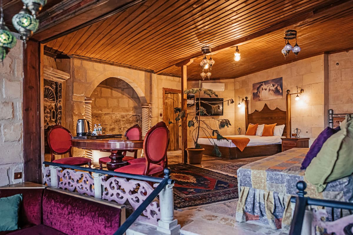 A cozy room with a wooden ceiling, a bed with orange and white bedding, a small table with chairs, and a decorative wall hanging.
