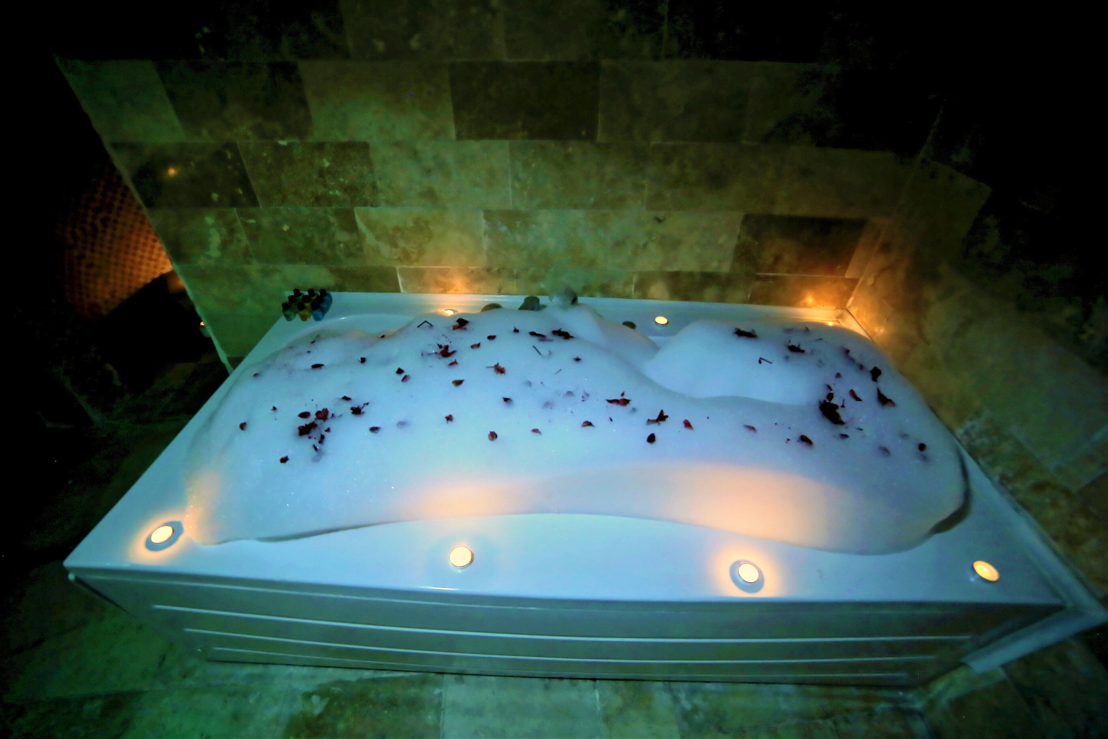 Ein rechteckiges Whirlpoolbecken mit weißem Innenraum, umgeben von Steinmauern und beleuchtet von vier kleinen Lichtern.