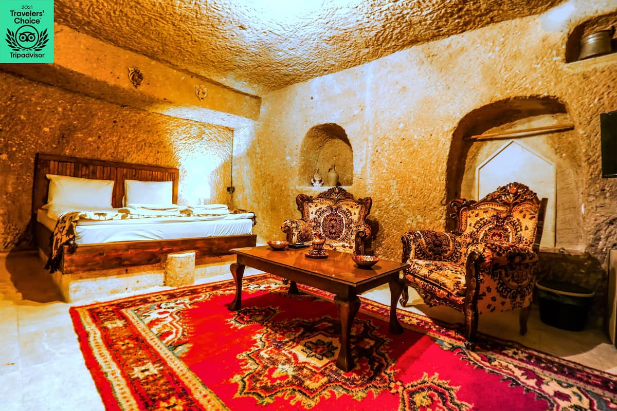 A traditional room with a bed, a wooden table, and two ornate chairs.