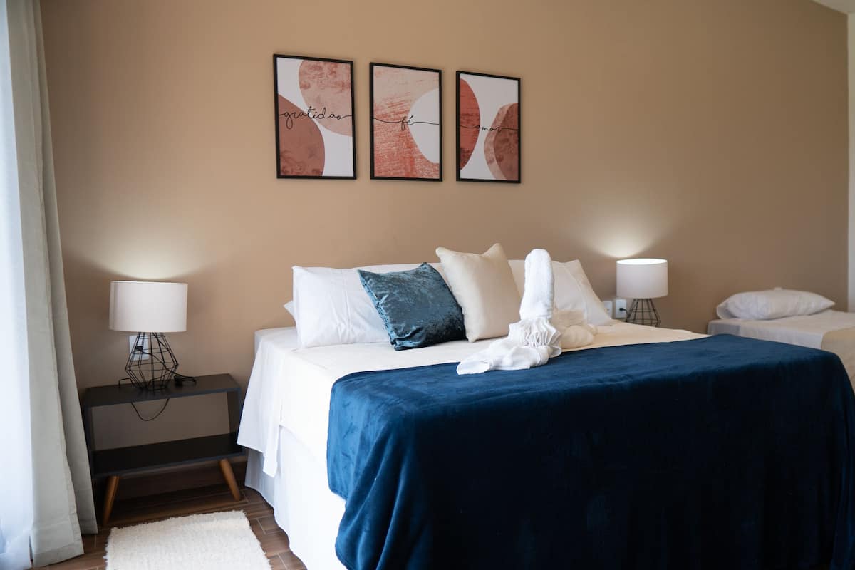 A hotel room with a bed, two bedside tables, a nightstand, a desk, and a chair. There are three framed artworks on the wall.