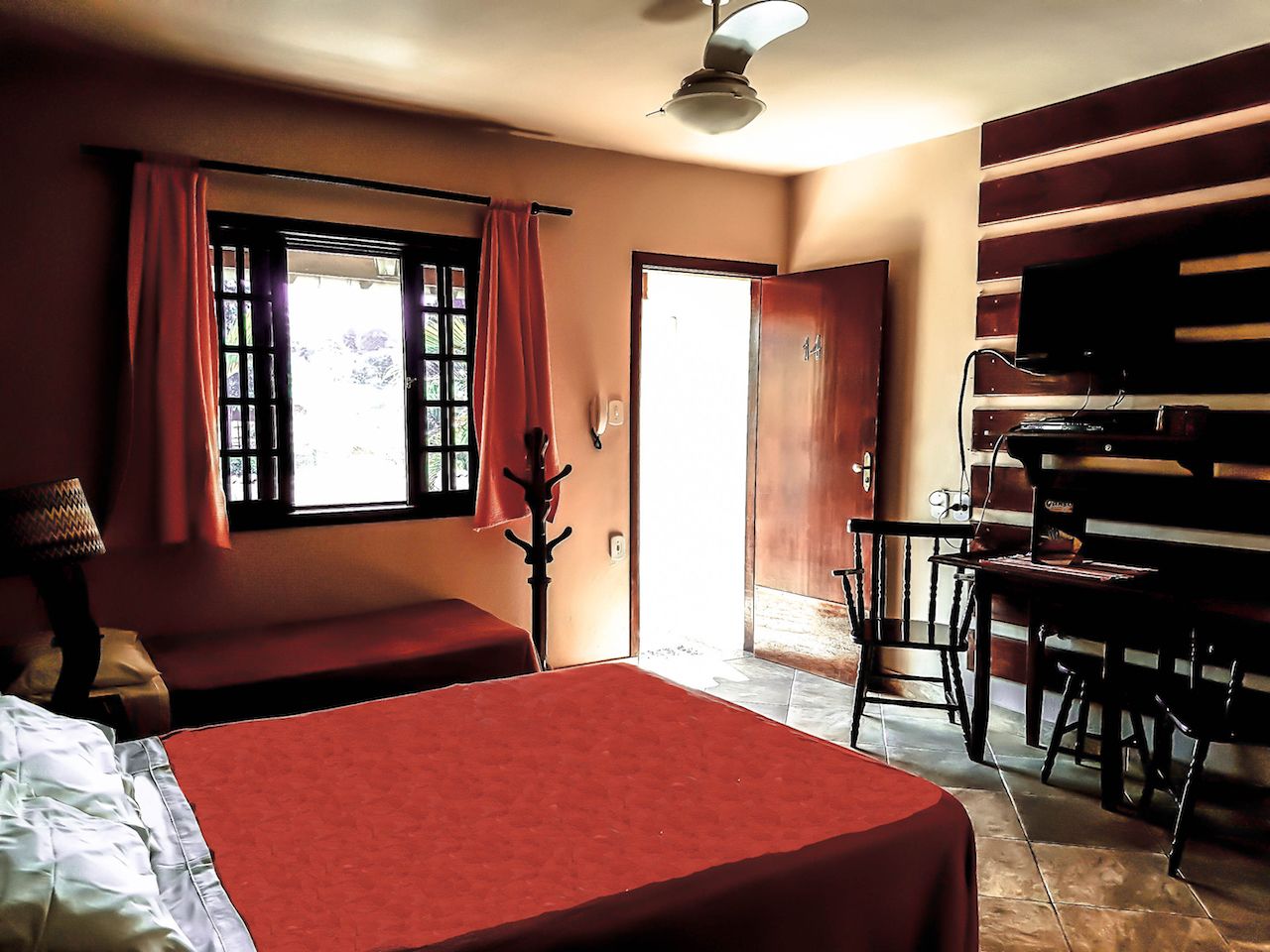 Una habitación con dos camas, un escritorio, una silla, un perchero y una puerta que da al exterior.