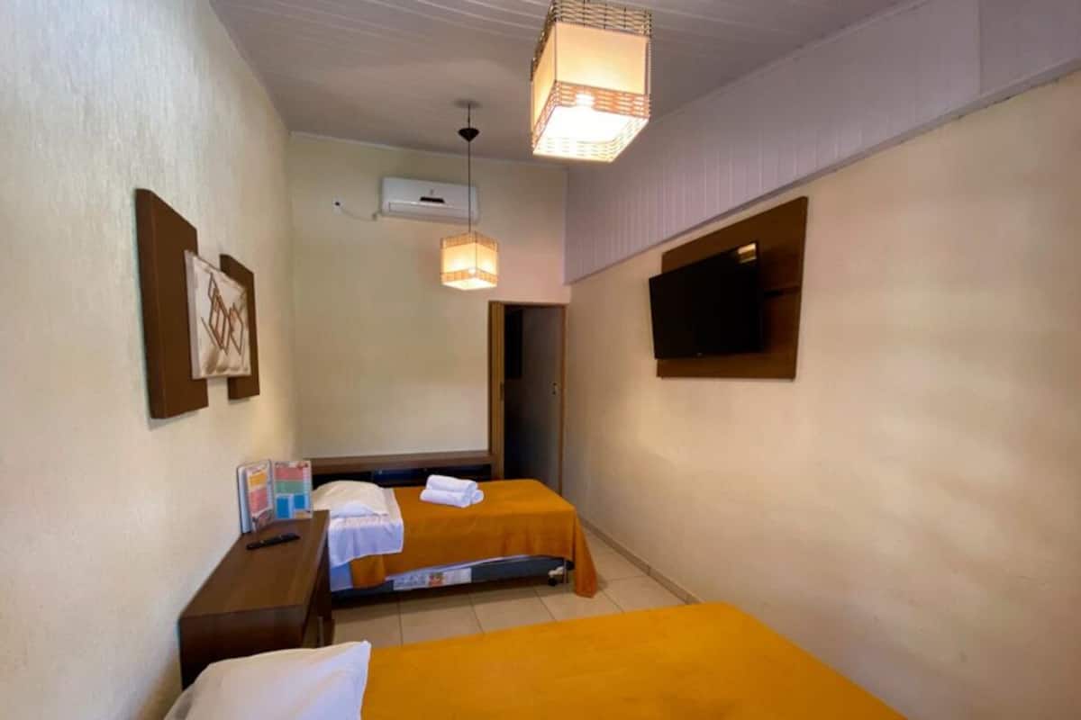 A hotel room with two beds, a desk, a television, and a hanging light fixture.