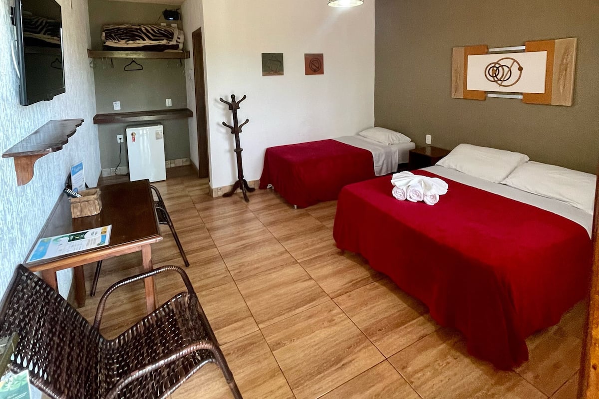 A compact hotel room with two beds, a small kitchenette, a dining area with a table and chairs, and a ceiling fan.