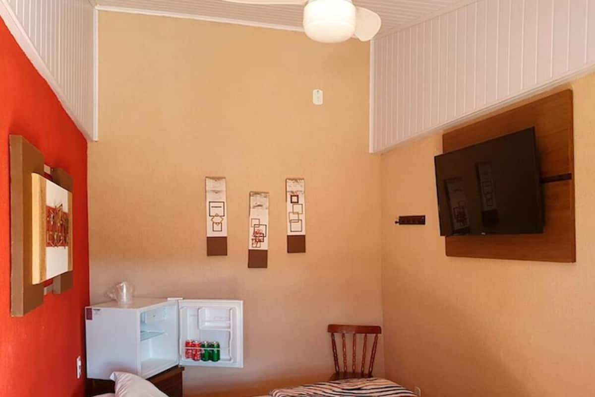 A compact room with a white ceiling, a wall-mounted TV, a refrigerator, and a chair.