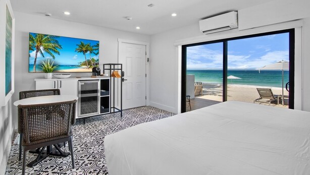 A hotel room with a bed, a desk with a computer, a chair, and a view of the beach. - Seaside at Anna Maria Island Inn (Bradenton Beach)