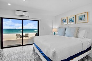 A hotel room with a large bed, a sliding glass door to the beach, and a ceiling air conditioner.