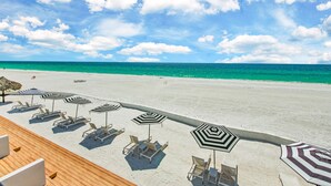 A beach with lounge chairs and striped umbrellas, a wooden deck, and a view of the ocean. - Seaside at Anna Maria Island Inn (Bradenton Beach)