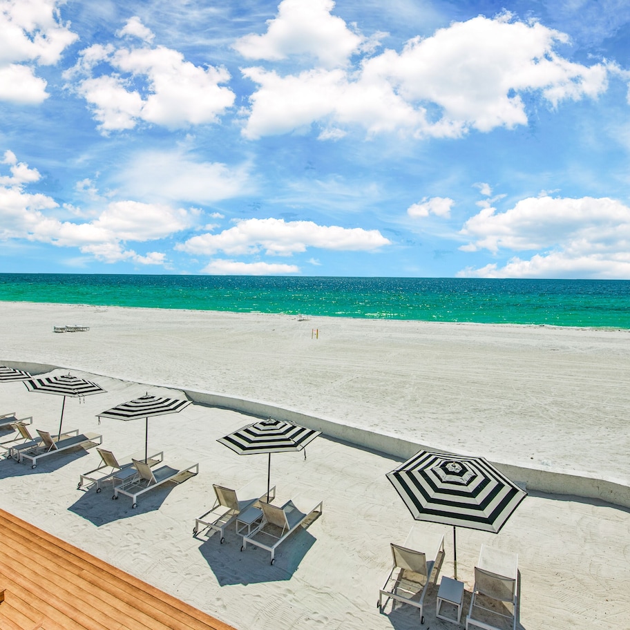 A beach with lounge chairs and striped umbrellas, a wooden deck, and a view of the ocean.