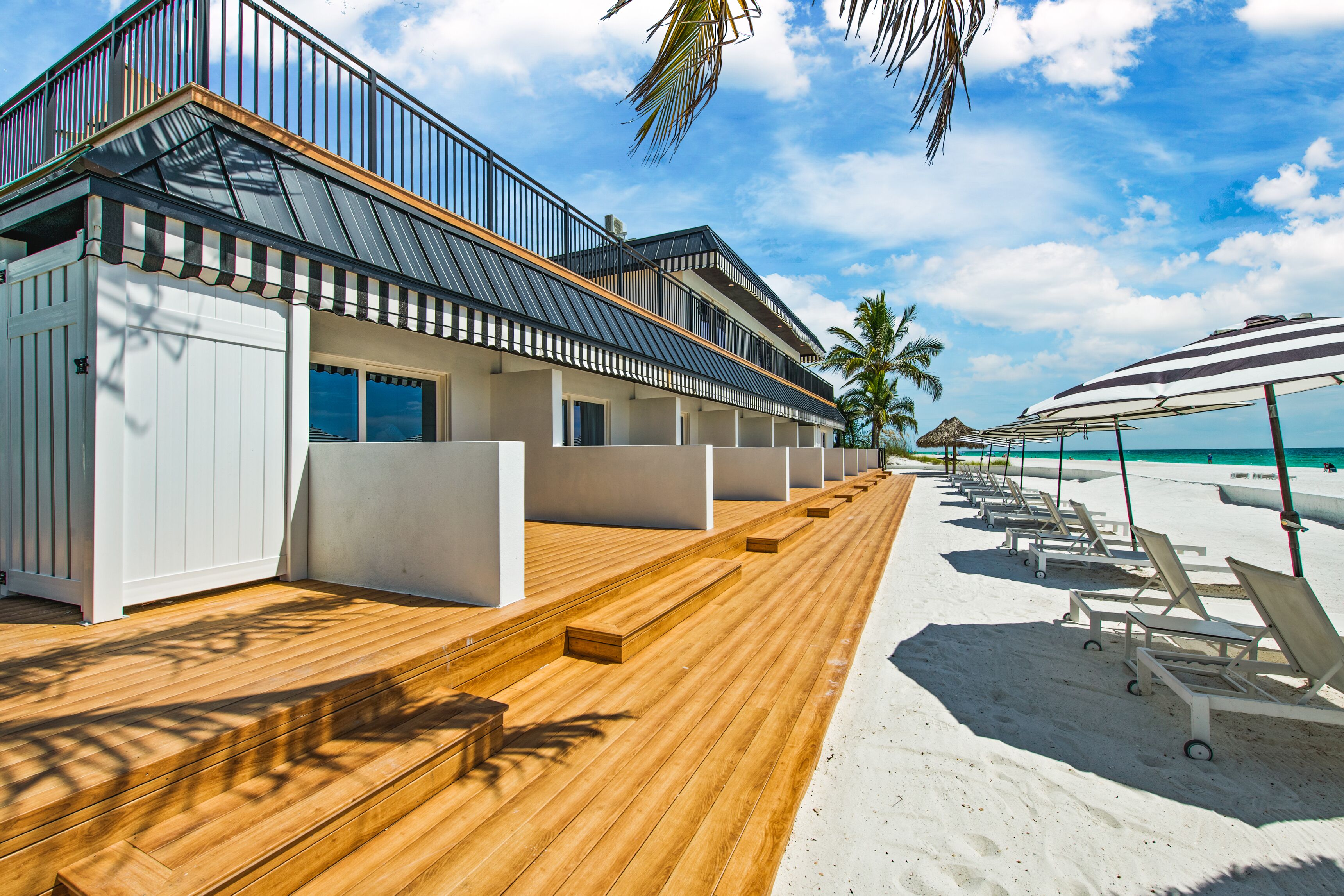 A beachfront hotel with wooden deck seating, a poolside area, and a clear view of the ocean.