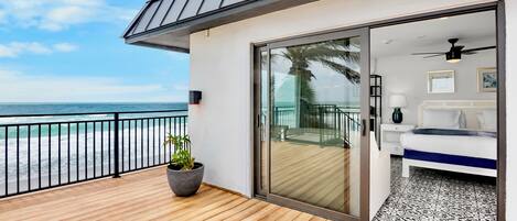 A modern room with a large sliding glass door leading to a balcony with a view of the ocean.