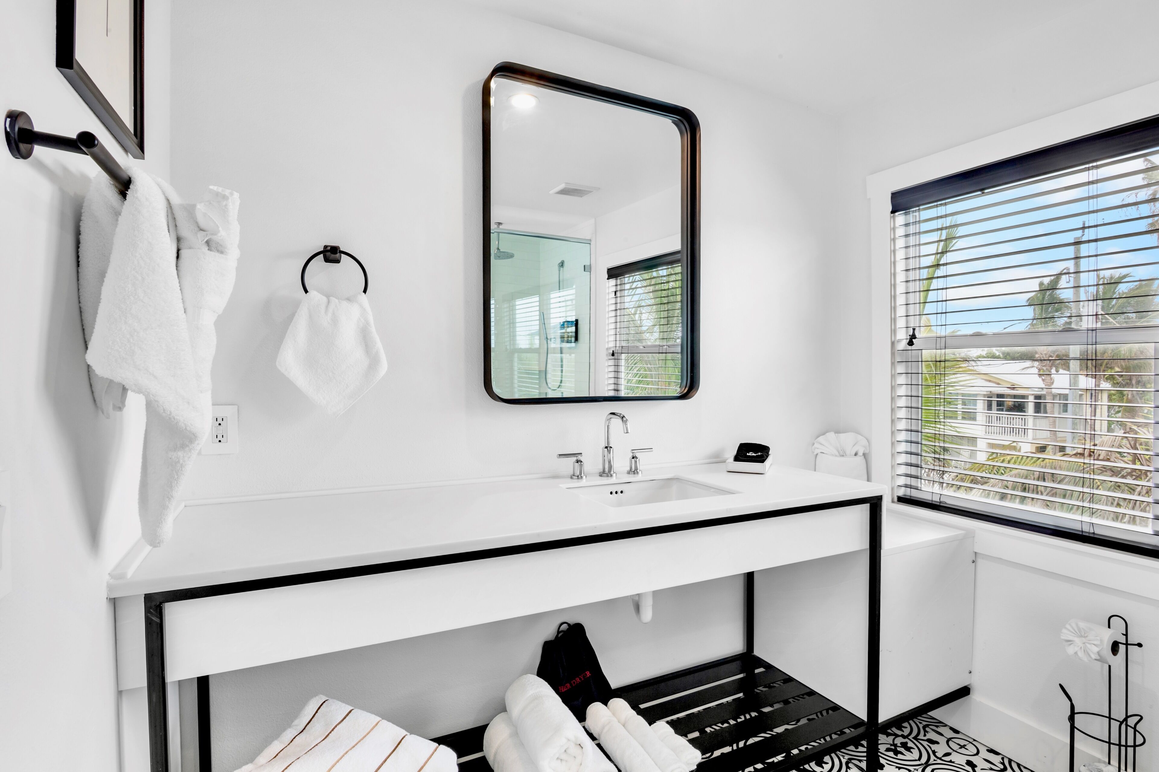 Un baño moderno con un lavabo blanco, un espejo y una ventana con persianas.