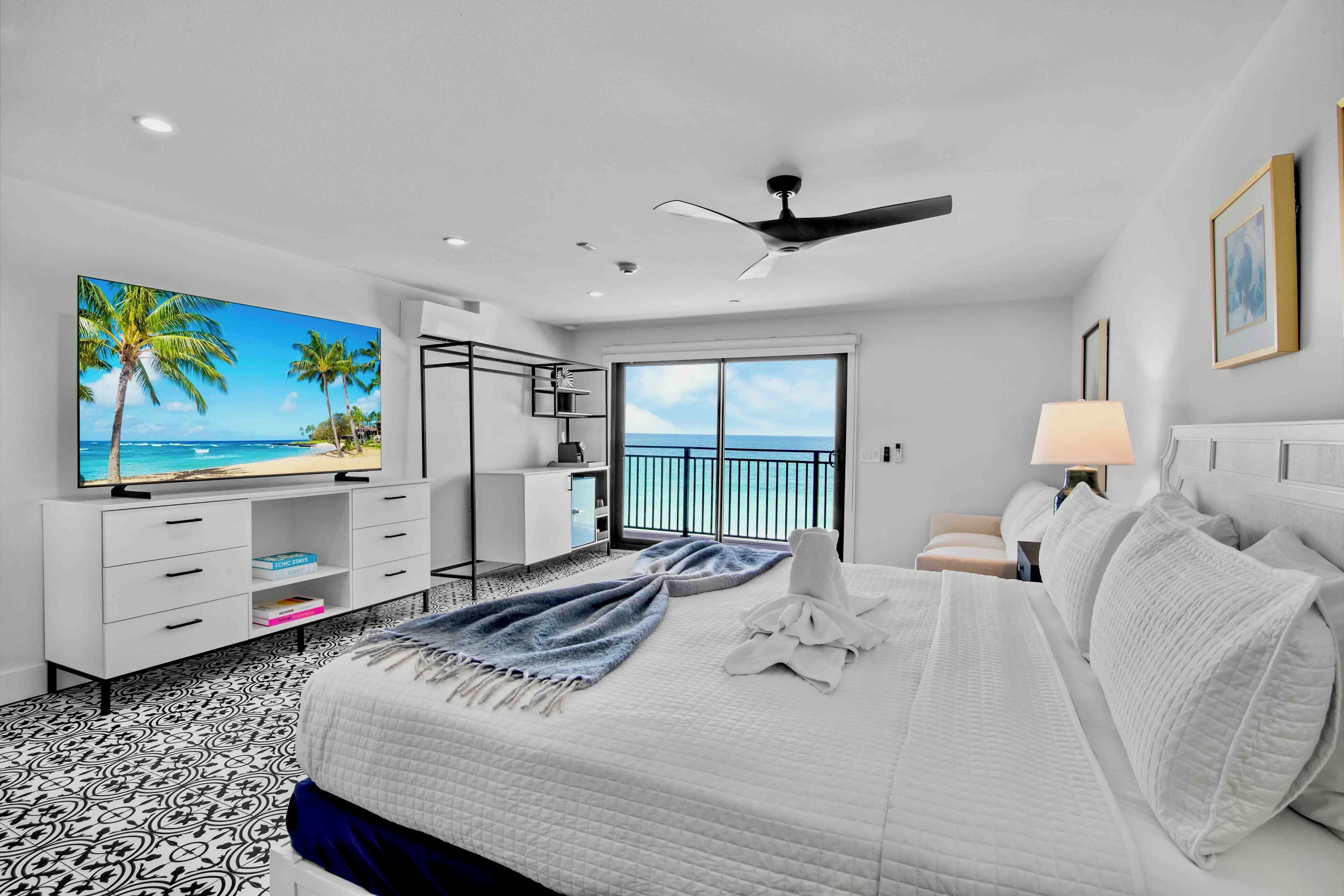 A hotel room with a bed, a TV, a balcony with a view, and a ceiling fan.
