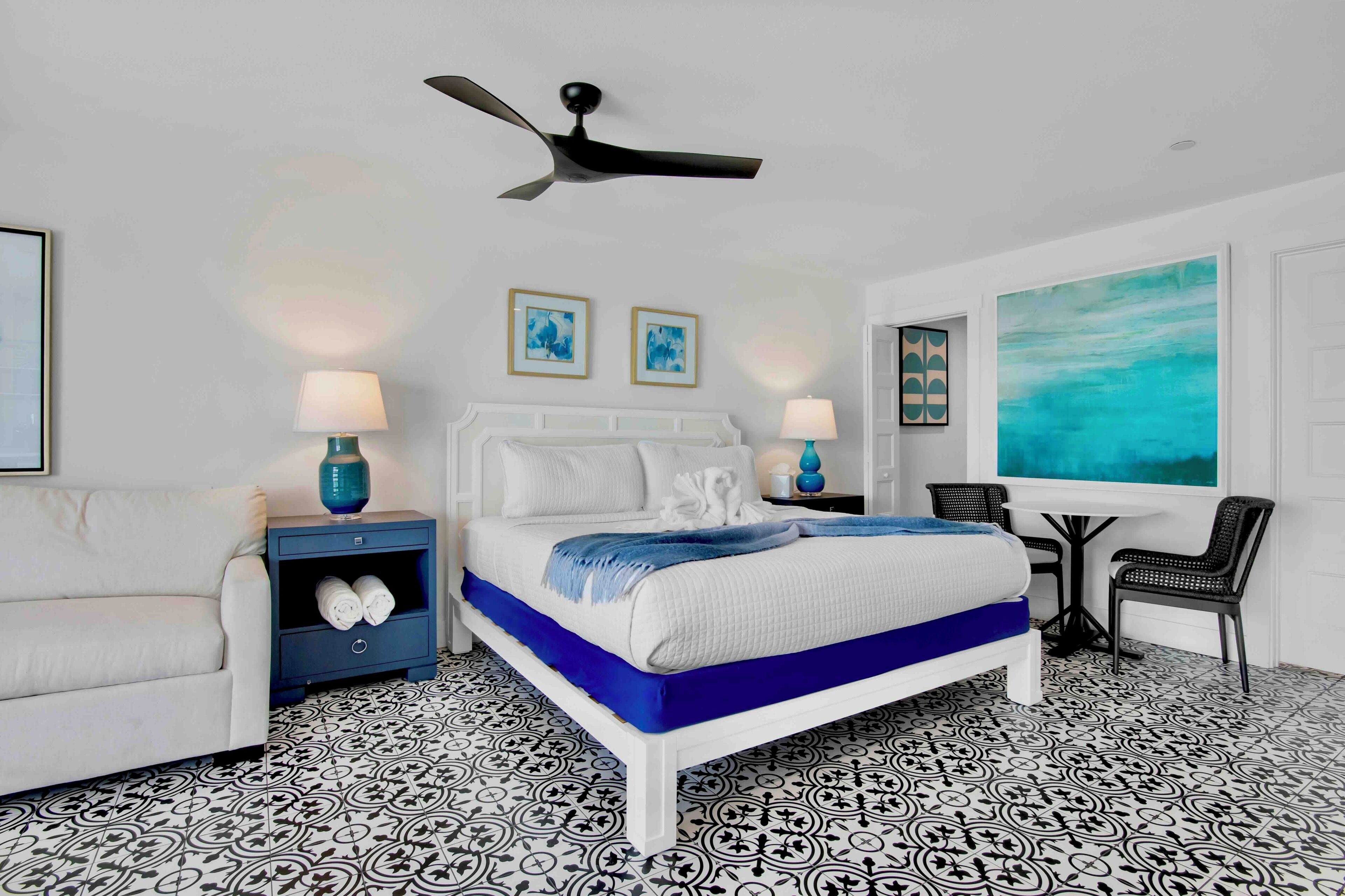 A modern bedroom with a bed, nightstands, a chair, a table, and artwork on the walls.