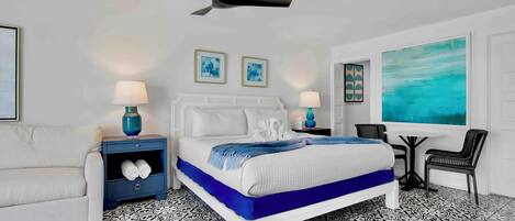 A modern bedroom with a bed, nightstands, a chair, a table, and artwork on the walls.
