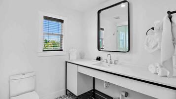 A modern bathroom with a white sink, a large mirror, and a window with blinds.