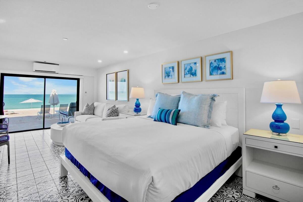 A hotel room with a large bed, two bedside tables, a desk, and a view of the beach.