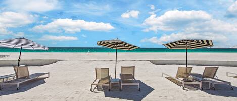 A beach with lounge chairs and striped umbrellas.