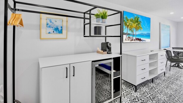 A modern room with a white cabinet, a black metal shelf, a framed abstract painting, a potted plant, and a beach scene painting. - Seaside at Anna Maria Island Inn (Bradenton Beach)
