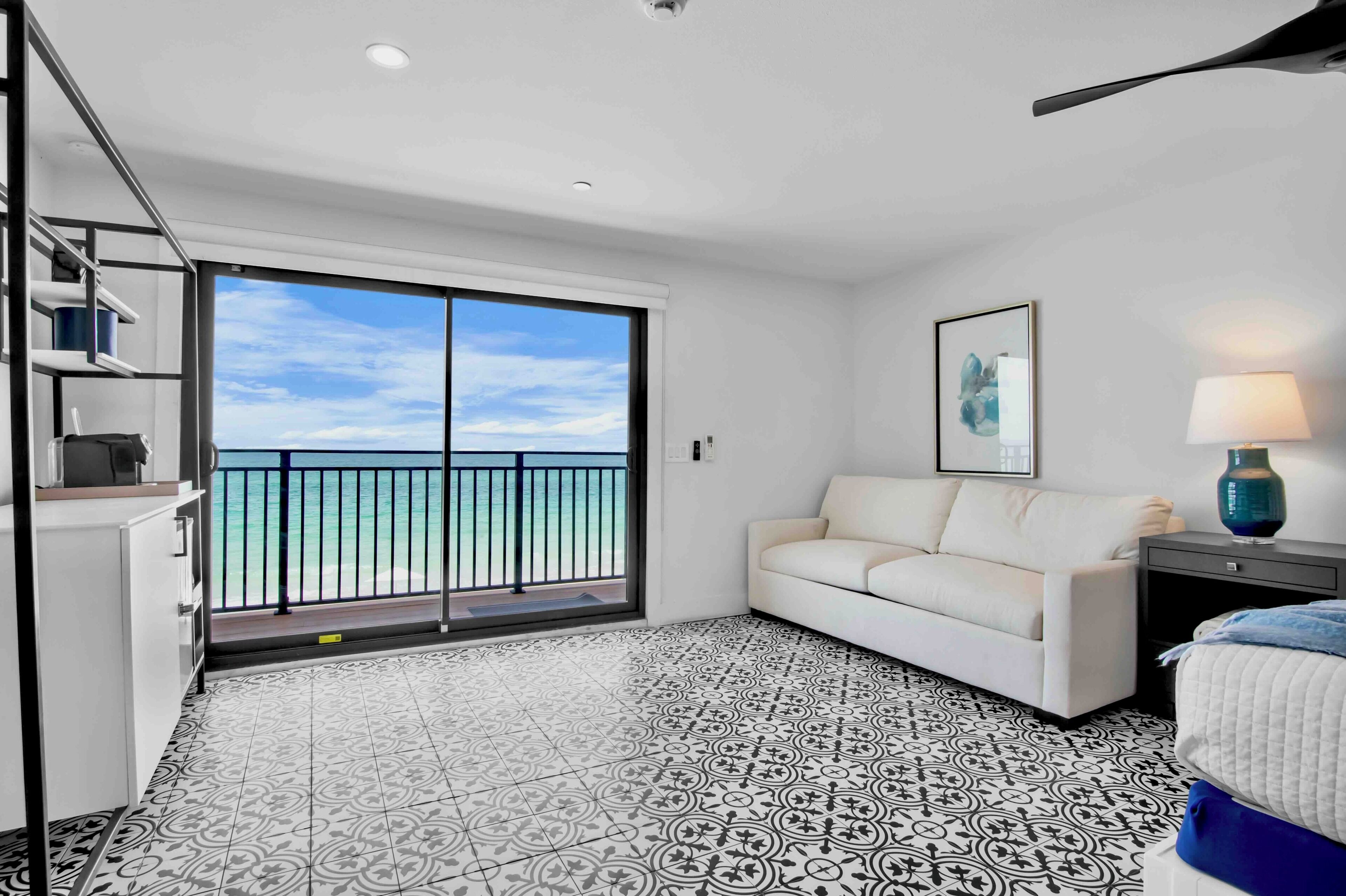 Une chambre d’hôtel avec un balcon, un canapé blanc, un sol à motifs et un tableau encadré au mur.