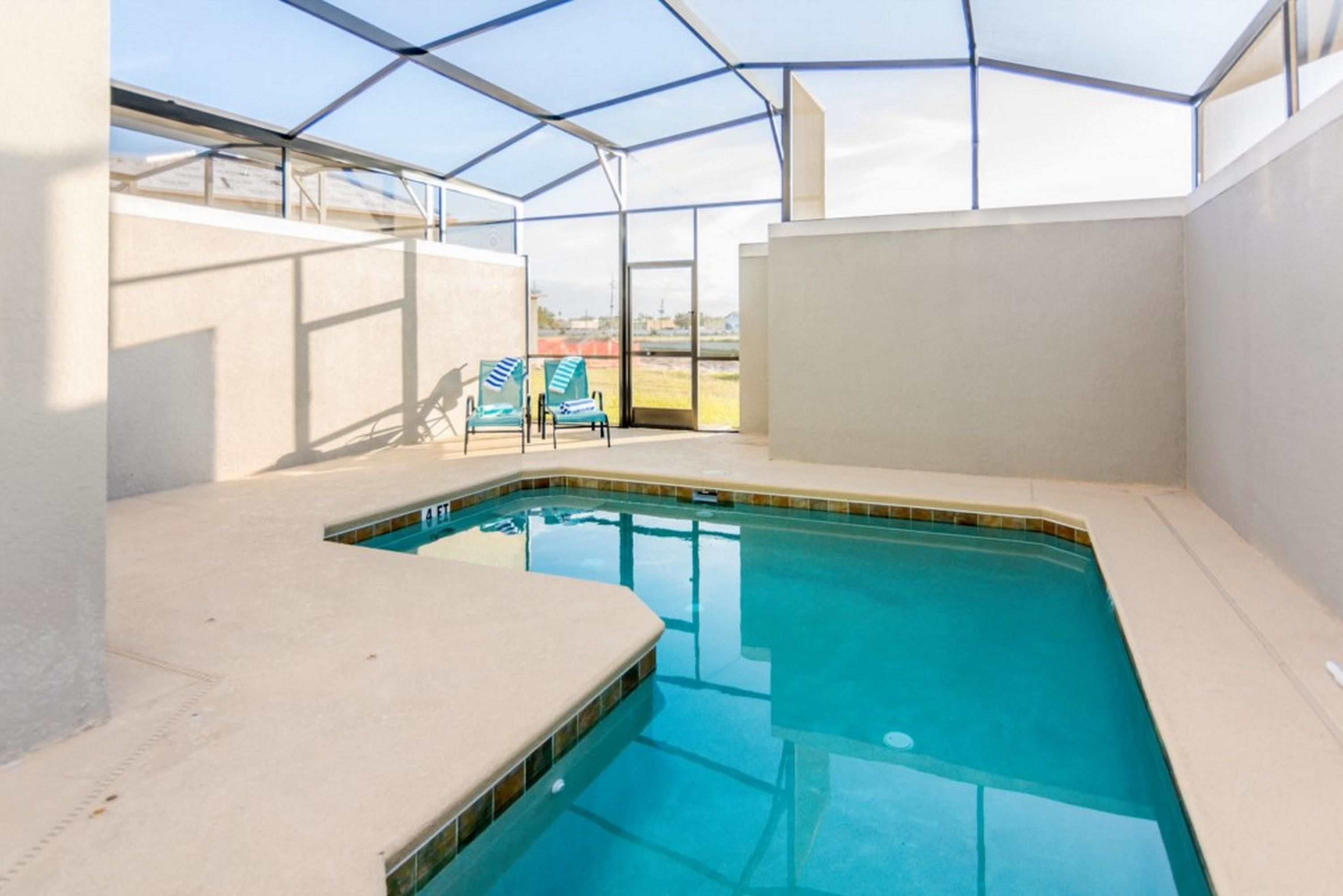 A swimming pool with a glass enclosure, two blue chairs, and a view of the landscape.