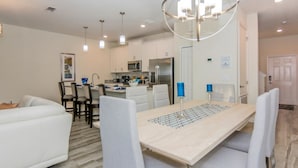 A modern kitchen with white cabinets, a central island, and a dining area with a light-colored table and white chairs. - Amazing Townhome with private pool SL3054 (Kissimmee)