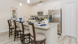 A modern kitchen with white cabinets, a stainless steel refrigerator, a granite countertop, and a central island with bar stools. - Amazing Townhome with private pool SL3054 (Kissimmee)