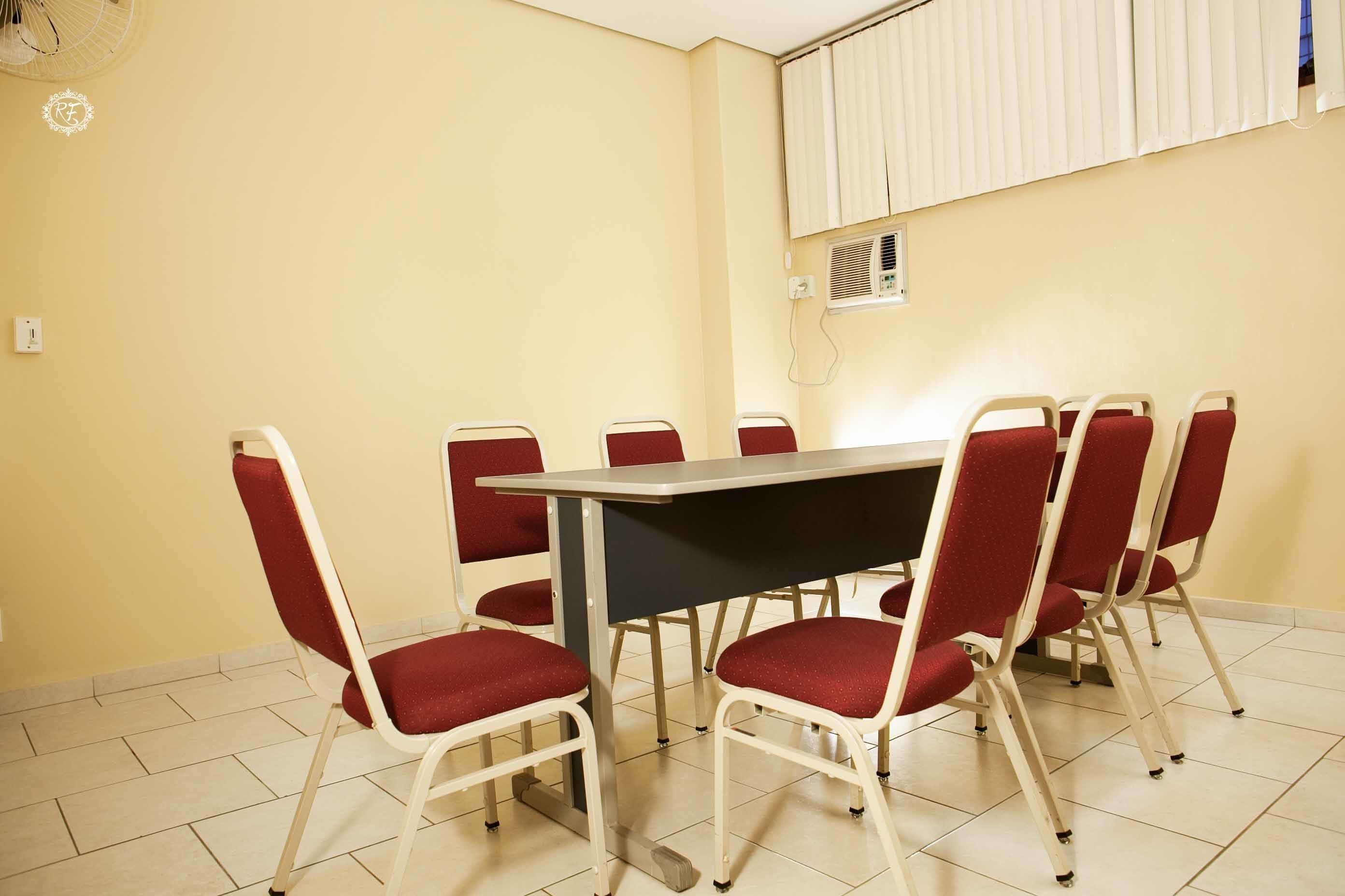 Une salle de conférence avec une table rectangulaire et six chaises rouges.