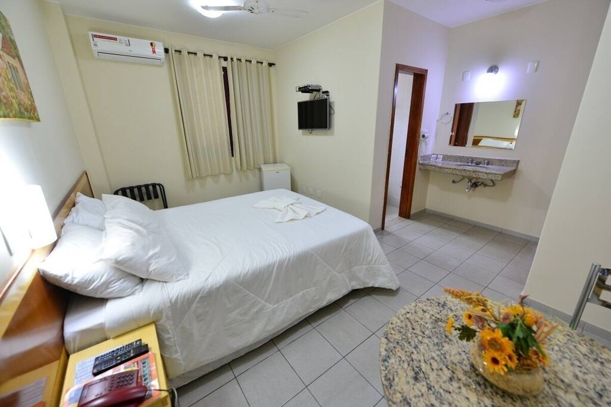 A hotel room with a bed, a bedside table with a book, a TV, a bathroom with a sink and mirror, and a ceiling fan.
