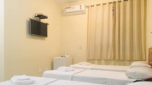 A hotel room with two single beds, a TV mounted on the wall, an air conditioning unit, and a window with curtains. - Hotel Vind's Plaza (Caratinga)