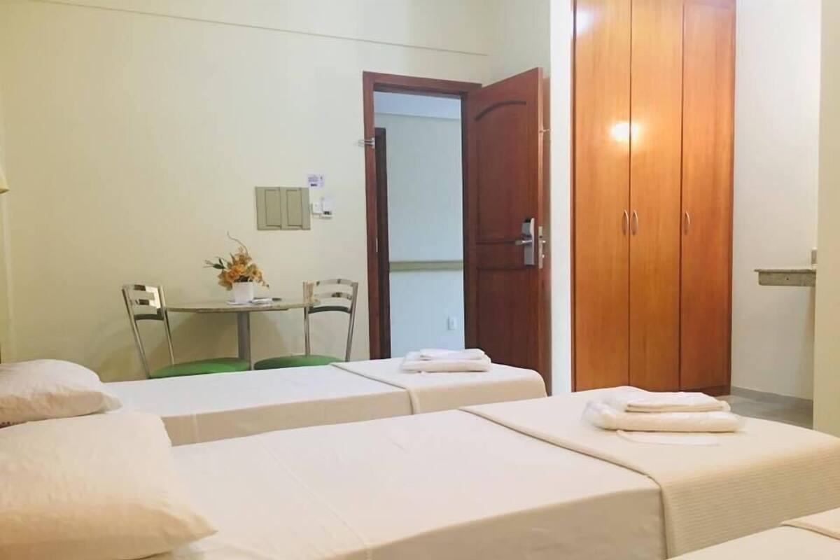 A hotel room with two single beds, a small table with chairs, a wooden wardrobe, and a door leading to another room.