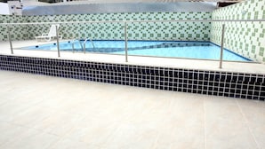 A swimming pool with a tiled deck and a metal railing. - Hotel Vind's Plaza (Caratinga)