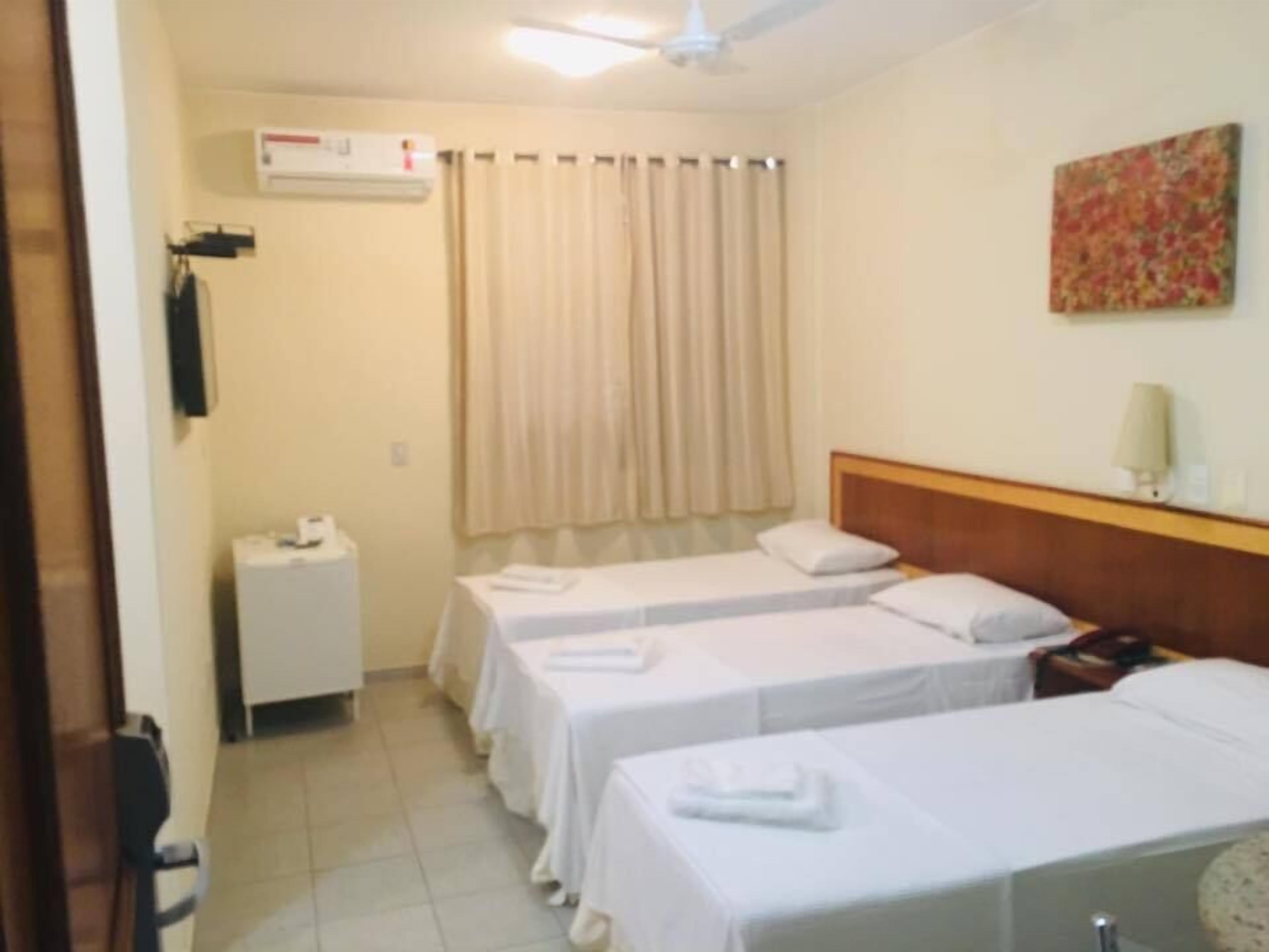 Camera d'albergo con due letti, una ventola a soffitto, un condizionatore d'aria, un tavolino con un telefono, una lampada e un quadro appeso al muro.