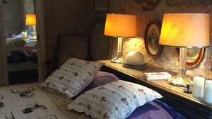 Ein Schlafzimmer mit einem Bett, zwei Lampen, einem Spiegel und einer Wand mit gerahmten Bildern und einer Uhr.