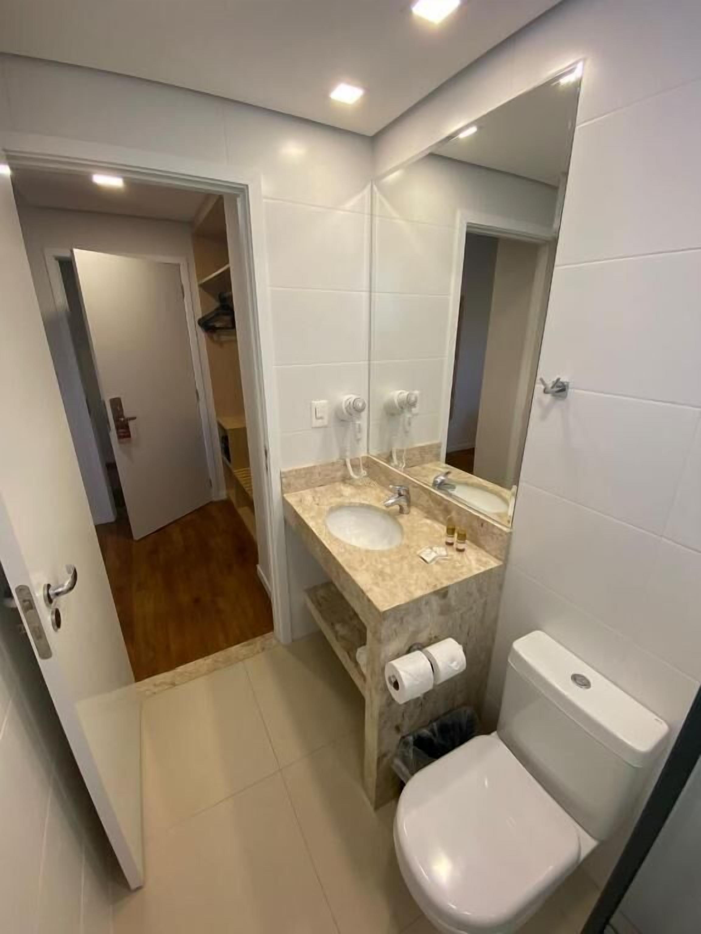 Une salle de bain avec des toilettes blanches, un lavabo doté d’un plan de travail en marbre et un miroir.