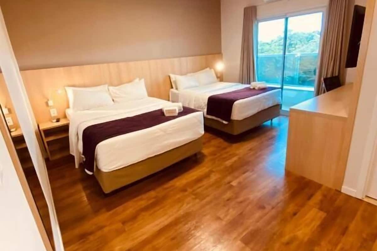A hotel room with two beds, a wooden floor, a large window, and a balcony.